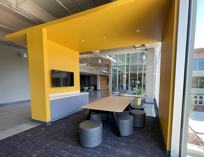 Tables and sitting area under an indoor yellow roof at the Student Organizations Hub.